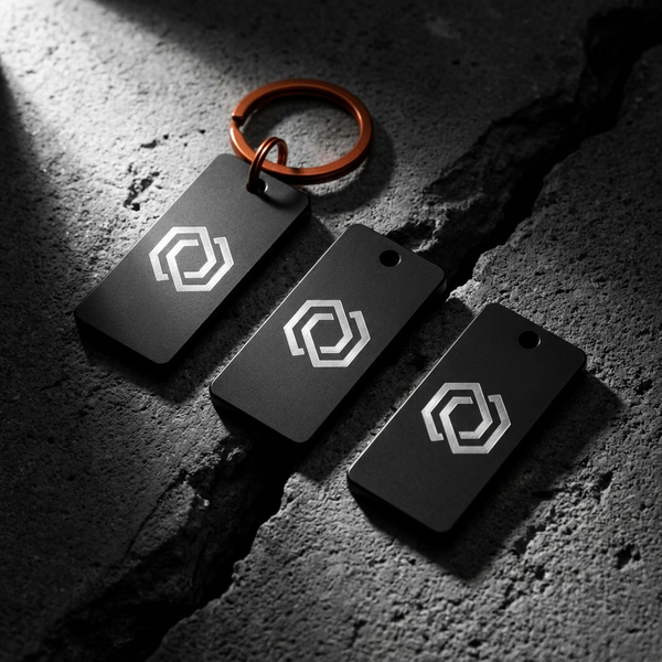 Three laser-engraved black metal keychains on dark concrete